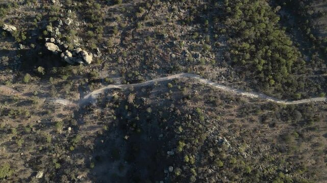 Dry trail cutting through rocky forested terrain in valle de los monjes, aerial view