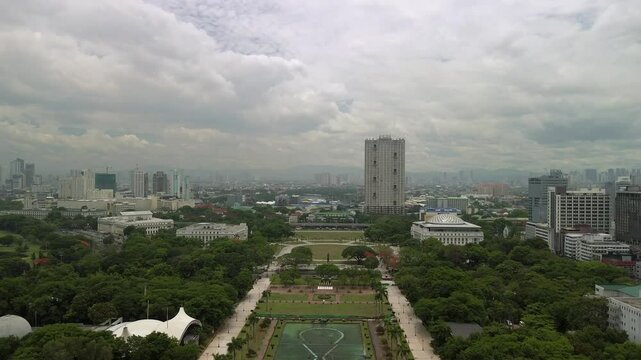 Aerial view along Rizal Park in Manila showing symmetrical lawns pathways monuments tree lined grounds and distant skyline under cloudy daylight