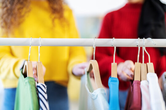 Two individuals are browsing a selection of colorful clothes hanging neatly on a rail with wooden hangers. They are engaged in the process of shopping for new garments.