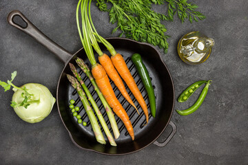 Fresh carrots with green tops, green pepper pod and asparagus in frying pan.