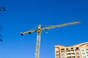 A construction crane and a part of an unfinished house made of ceramic bricks against ablue sky.