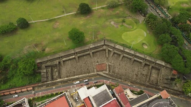 Intramuros fortress wall and adjoining park grounds form a geometric overhead pattern beside roads and red roofed buildings in Manila