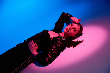 Stylish young woman poses artistically in studio lighting with vibrant backdrop colors