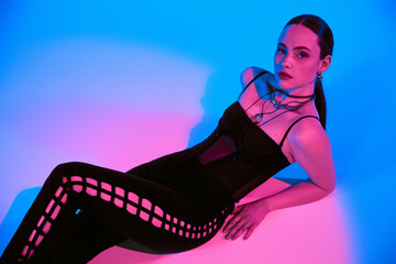 Stylish young woman poses against vibrant pink and blue lighting