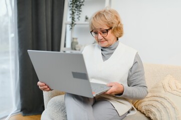 Senior woman using laptop , sitting on sofa at home interior