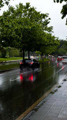 Rainy urban street with cars and reflective puddles on overcast day