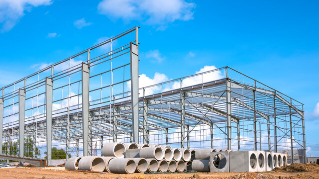Metal structure of industry warehouse factory building with concrete drainage pipes on the ground in construction site against blue sky background, perspective side view 