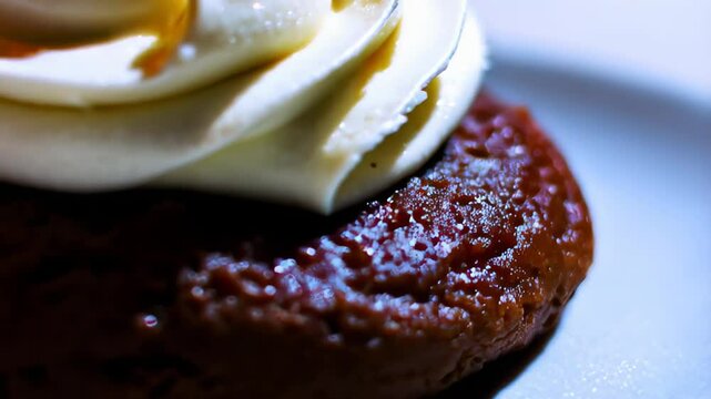 Small round chocolate pastry topped with a generous swirl of vanilla whipped cream and a glossy red maraschino cherry, served on a white plate.