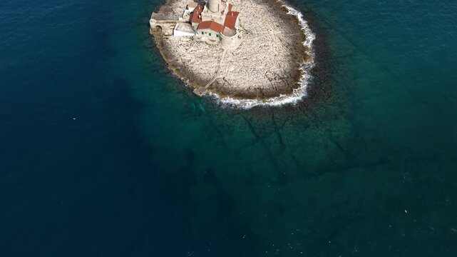 Top-down drone view of a circular rocky island featuring the historic Porer Lighthouse in the center, near Pula, Croatia