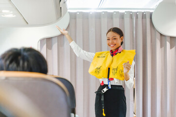 Smiling flight attendant demonstrating safety instructions with a life vest during pre-flight briefing onboard. Promotes airline safety, passenger care, and travel service professionalism.