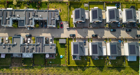 Rows of single-family houses on the city outskirts, featuring solar panels and green gardens,...