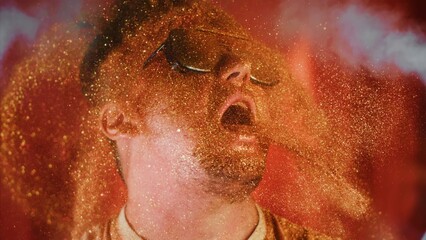 Crazy fun man sprinkles himself with sparkle particles. Fun photo funny face, tongue out. Comical funny portrait guy in sunglasses pouring on face and mouth gold glitter in super best joke perfomance