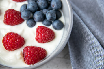 Gray bowl and natural yogurt with red andf blue berries on the stone marble table.