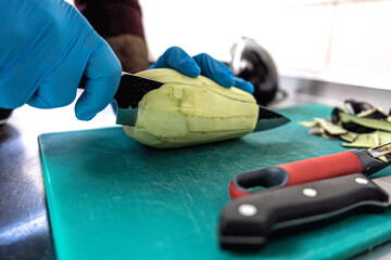 Chef slicing peeled eggplant on green board wearing gloves in professional kitchen