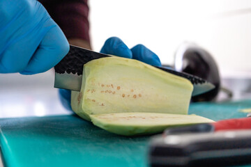 Chef slicing peeled eggplant to reveal seeds on green cutting board