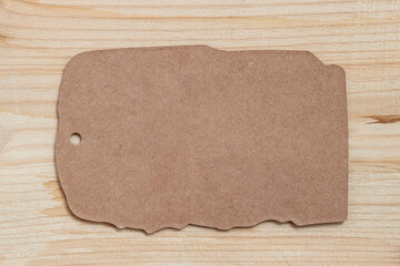 Natural mockup of blank cardboard tag on wooden background. Blank kraft paper tag on wooden background with rough torn edges, hole for string. Concept of vintage label, price tag. eco-friendly design