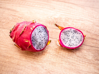 Sliced dragon fruit on wooden surface, showing white flesh with black seeds and pink skin. Exotic...