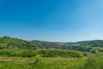 Endless green hills embrace a charming village under a bright blue sky on a sunlit day