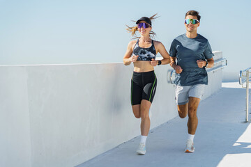 Couple enjoying an energizing morning run along a stunning waterfront promenade under clear blue skies