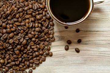 A light wooden table with a pile of roasted coffee beans on the left and a white cup filled with black coffee on top, with a few scattered beans. Ideal for coffee-themed designs.