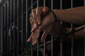 Hands of a prisoner behind prison bars on black background