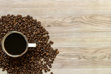 A mug of black coffee amidst a pile of coffee beans on a wooden background in the lower left corner.