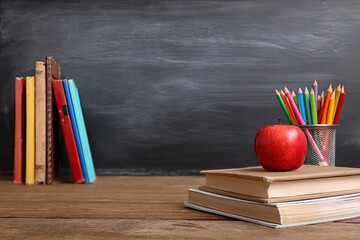 A rustic wooden desk holds books, colored pencils, and a red apple before a chalkboard
