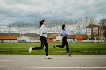 Two female friends running or jogging on stadium doing sport activities	
