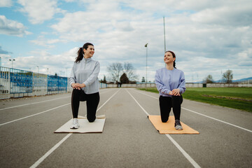 Two female friends stretching on stadium doing sport activities	
