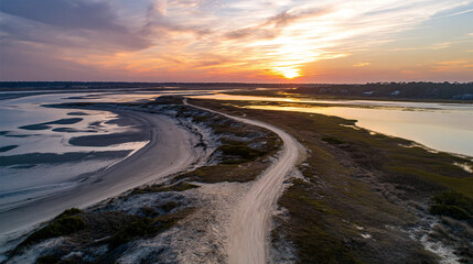 Winding Dirt Road Through Coastal Marshland Towards Distant Buildings at Golden Sunset with Reflective Tidal Pools