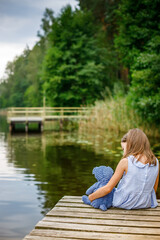 A serene and emotional scene of a young girl in a striped dress, contemplating by the water’s...
