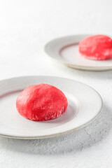 Traditional Japanese dessert mochi cake in thin pink rice dough on a plate on white textured background, open space