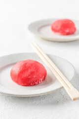 Traditional Japanese dessert mochi cake in thin pink rice dough on a plate with chopsticks on white textured background
