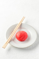 Traditional Japanese dessert mochi cake in thin pink rice dough on a plate with chopsticks on white...