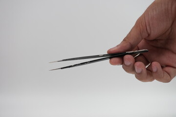 Hand with tweezers. Black precision tweezers. Gray stick. White background. Delicate work