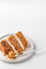 Homemade layered carrot cake with cream cheese, walnuts and spices on a plate with dessert fork