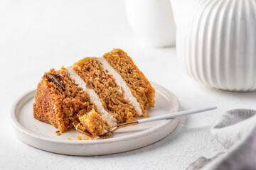 Homemade layered carrot cake with cream cheese, walnuts and spices on a plate with tea