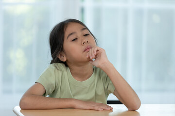 Young Girl in a Green Shirt Deep in Thought While Sitting at a Table in a Bright Indoor Environment