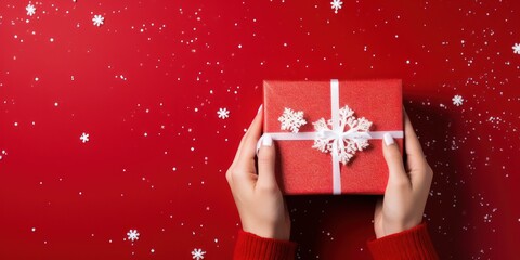 Woman holding a red gift box with a white ribbon and snowflakes on a red background with snowflakes