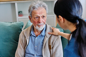 Doctor or nurse caregiver's hand giving support to sad lonely senior man at home or nursing home