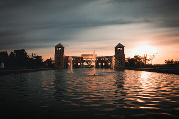 View of Tanguá Park in the city of Curitiba, Brazil, with the water mirror in the foreground, and the central structure with symmetrical towers in the background, illuminated by the sunset.