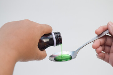 Green liquid medicine being poured into a spoon.