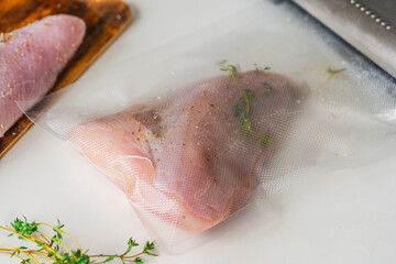 The process of vacuuming raw turkey meat with thyme on a light background.