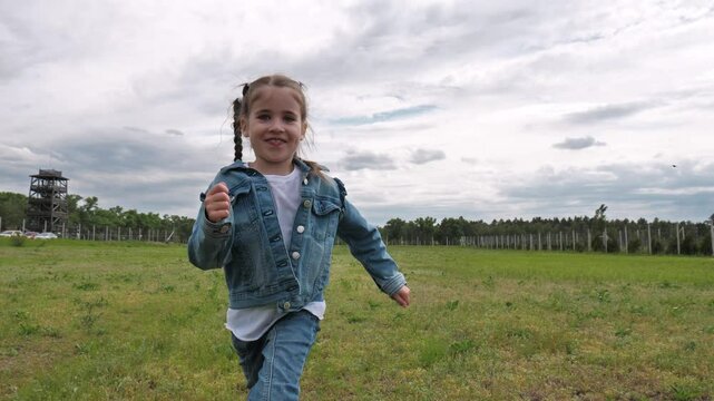 Portrait of happy little girl running on grass field, pigtails bouncing in slow motion. Cheerful girl playfully running in park and laughing. Happy childhood, activity and fun. Slow motion