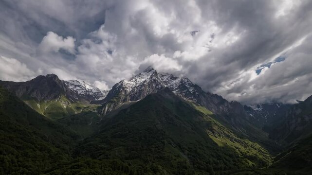 Wispy clouds hovering above snow-capped mountain range, casting gentle shadows across lush valley floor, revealing untouched wilderness bathed in soft sunlight