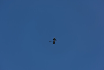 A lone helicopter soars through a vast, clear blue sky, a powerful silhouette against the open expanse. Evokes feelings of freedom and aerial dominance.