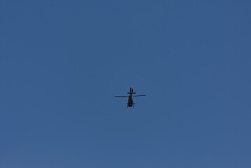 A lone helicopter soars through a vast, clear blue sky, a powerful silhouette against the open expanse. Evokes feelings of freedom and aerial dominance.