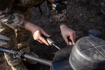 A soldier in camouflage adjusts sensitive equipment in a wooded area. The individual focuses...