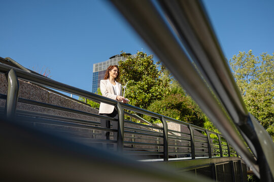 Businesswoman holding small wind turbine model on footbridge in urban setting
