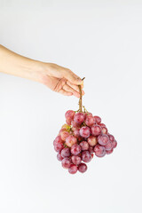A hand on a white background is holding a bunch of fresh grapes